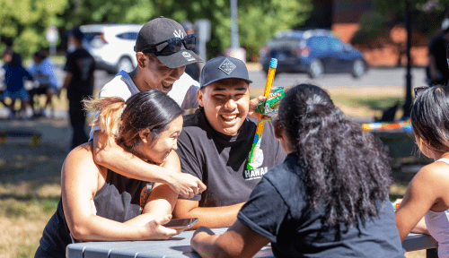 Students relax around a table outside in the sun