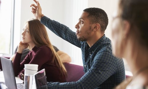 A student with peers on either side raises his hand in class.